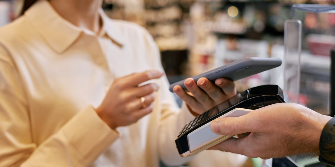 A smiling customer makes a contactless payment using a smartphone at a point-of-sale terminal in a modern café, illustrating the rise of digital and mobile payments.